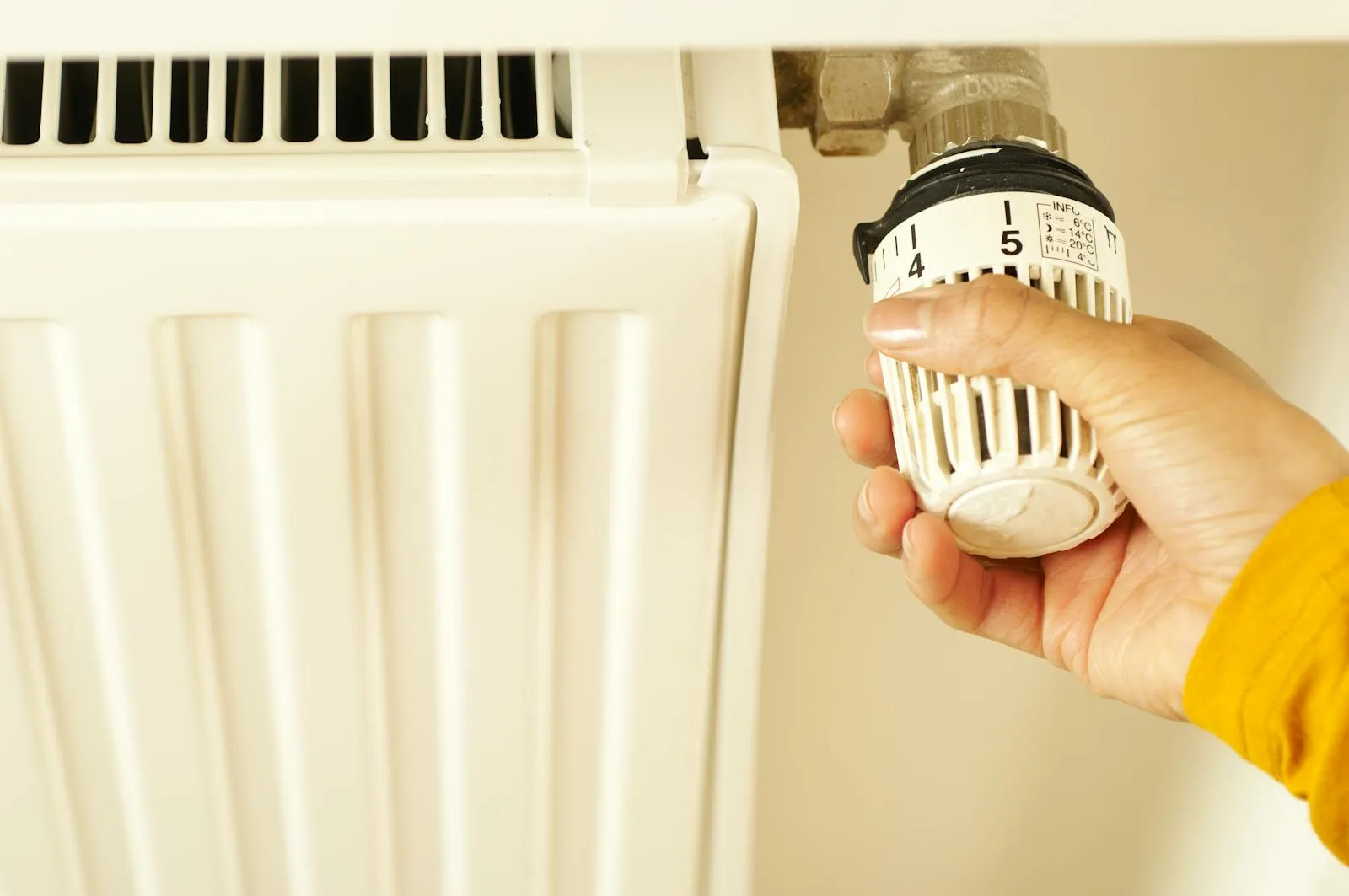 An engineer adjusting a thermostatic radiator valve — the survey checks whether each radiator can heat its room at heat pump temperatures.