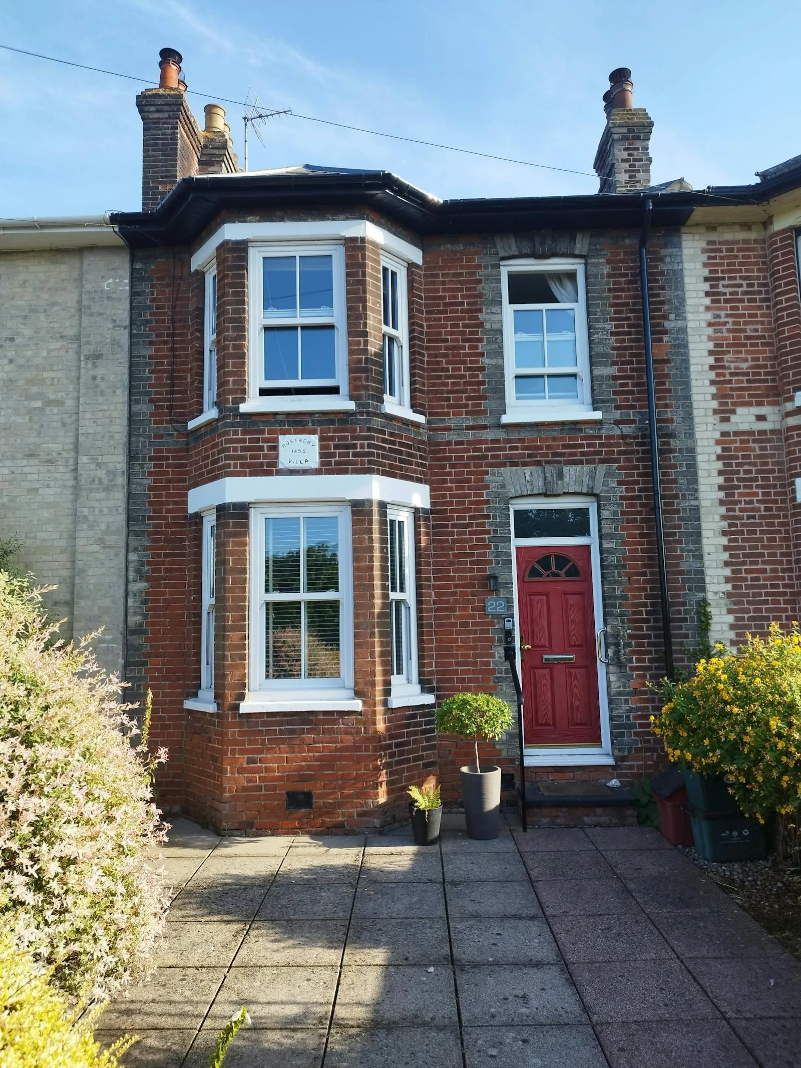 A red-brick Edwardian UK semi-detached house with white sash bay window and a red front door — period housing stock typical of the kind we install heat pumps in across inner-Bristol streets including Cotham.